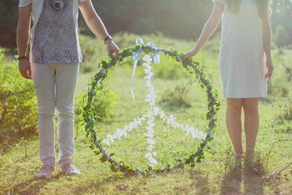 A couple holding a floral peace symbol outdoors in a sunny meadow.